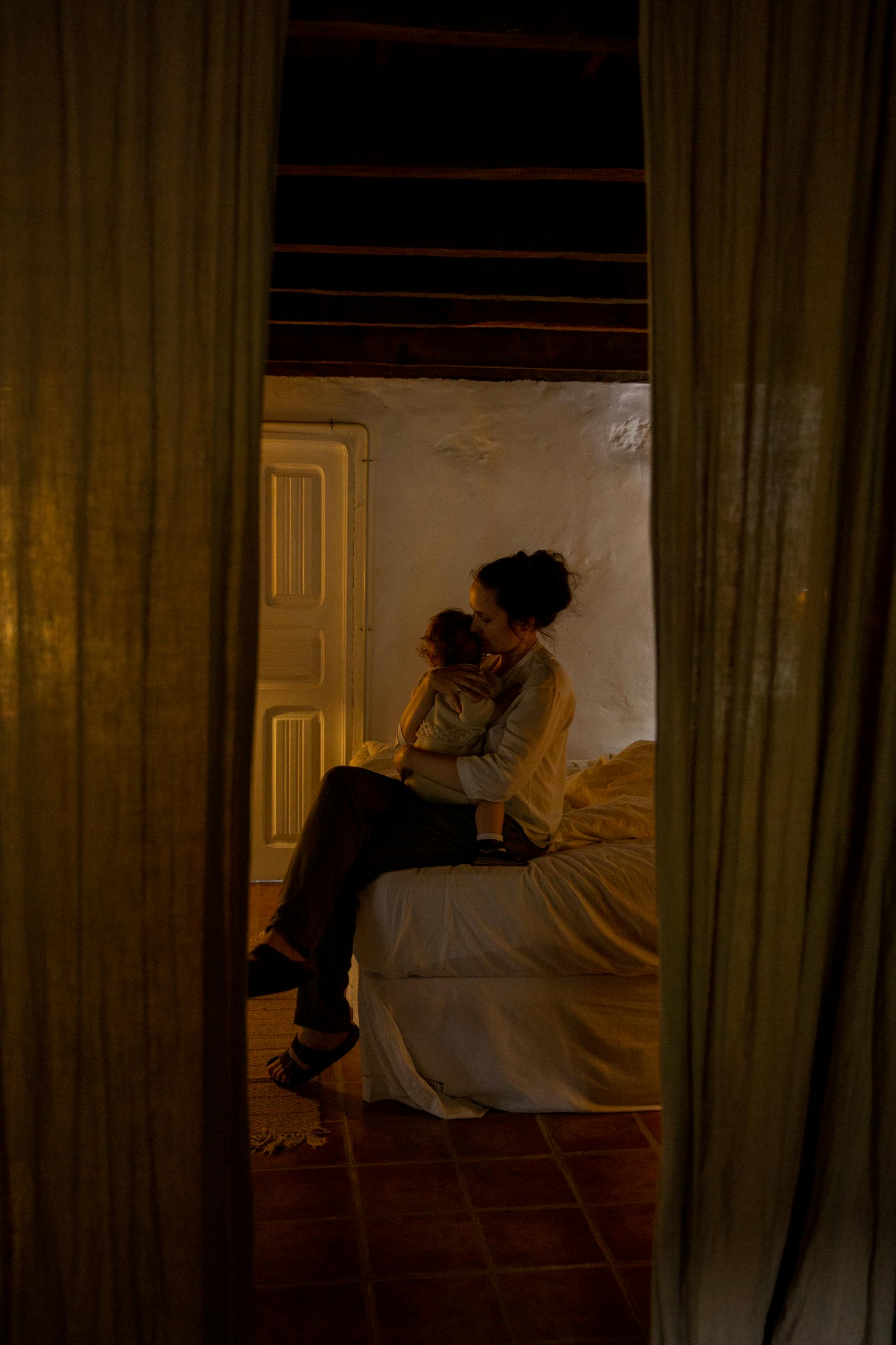 A cozy indoor scene of a mother holding her child on a bed, conveying warmth and affection.