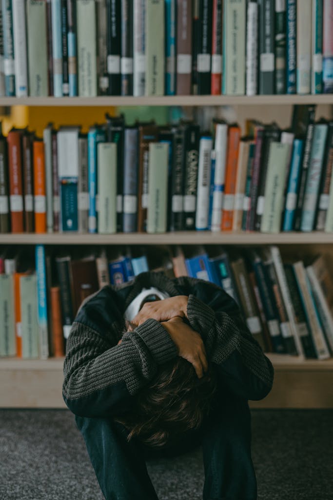 A young boy sitting on the floor in a library, looking distressed with bookshelves in the background.