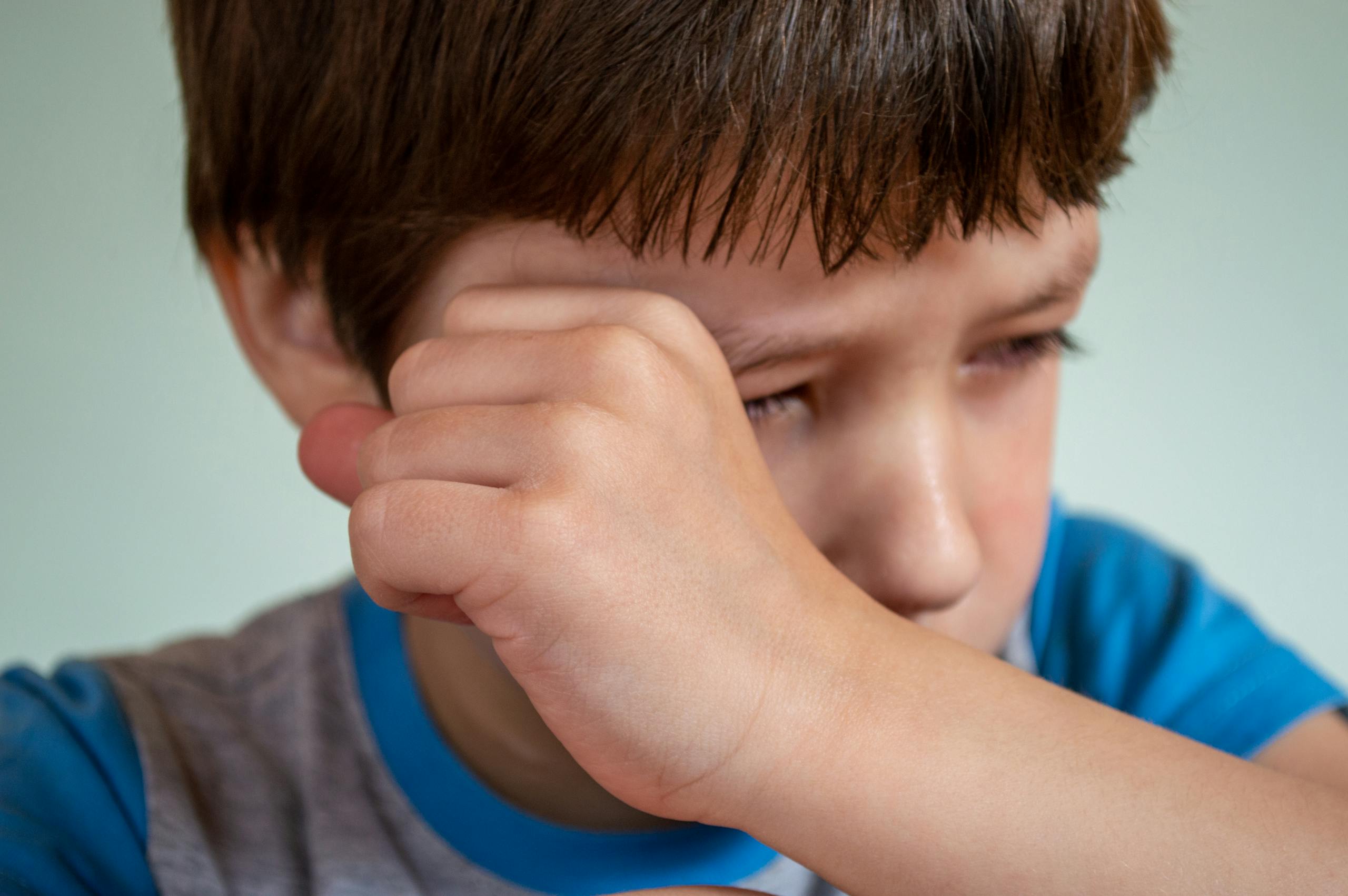 Close-up of a sad child wiping tears, expressing emotion and vulnerability indoors.