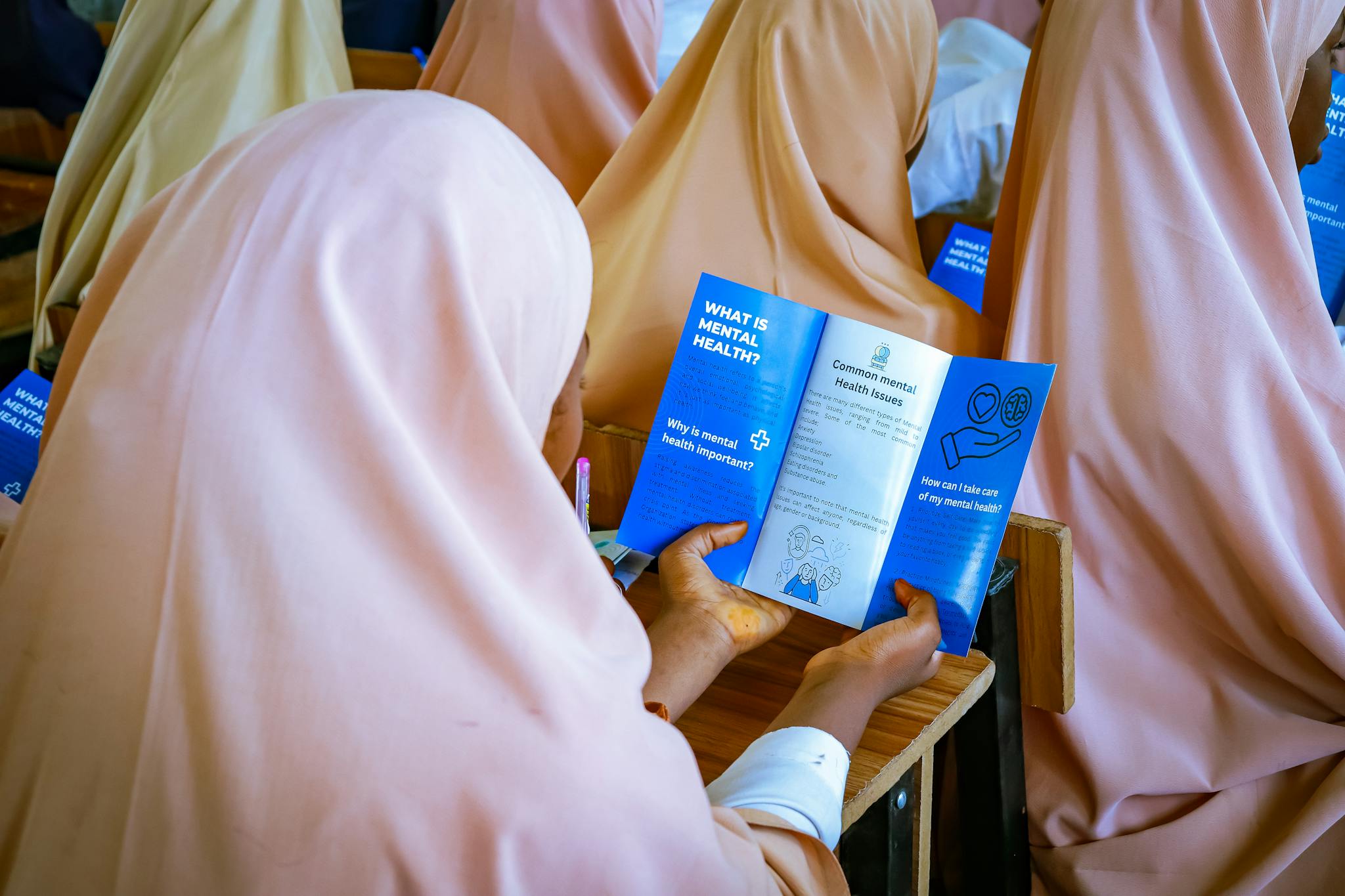 Women in classroom exploring mental health pamphlet, educating in Kaduna, Nigeria.